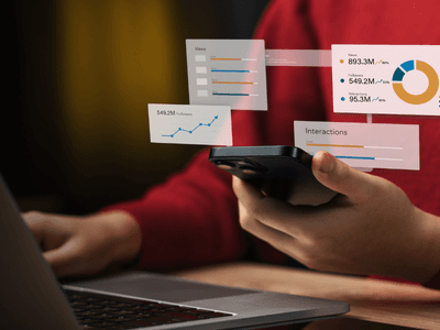 Person holding a smartphone while viewing analytics graphs on a laptop screen